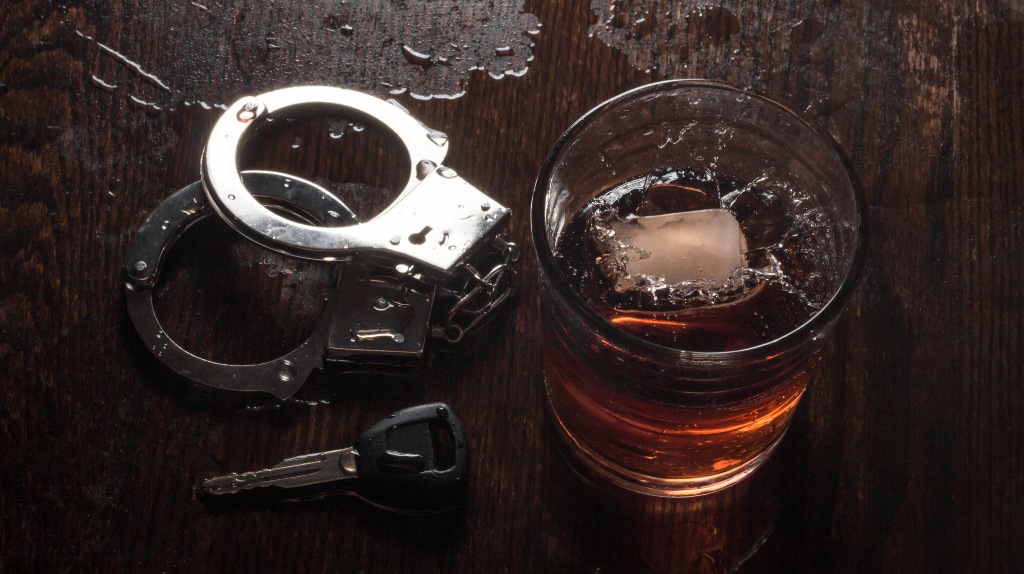 Rocks glass of whisky with handcuffs and car key