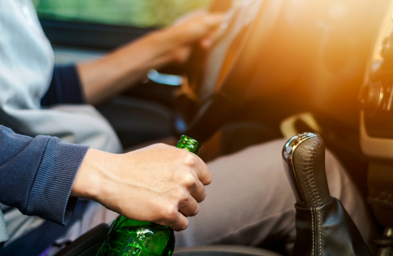 man holding alcohol bottle while driving a car