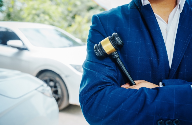 lawyer is standing in front of a car ad holding judge's gavel