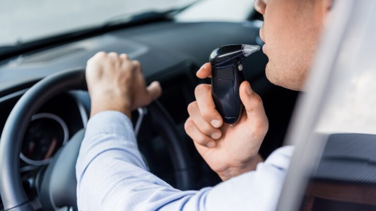 partial view of driver blowing into breathalyzer in car