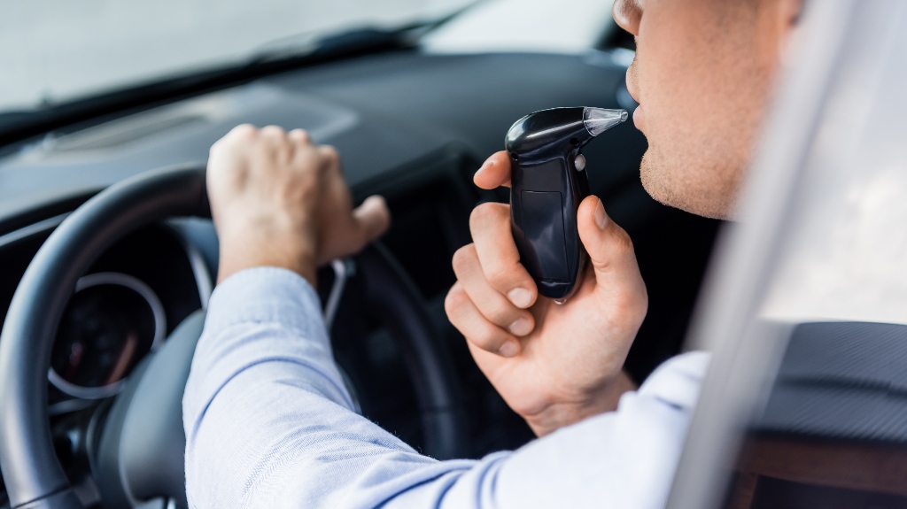 partial view of driver blowing into breathalyzer in car