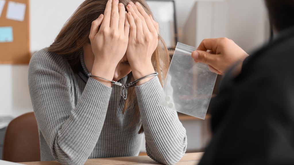 Handcuffed woman and detective with drugs during interrogation in office